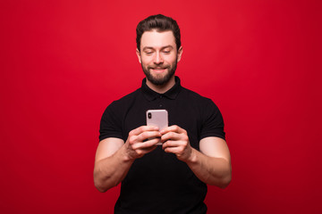 Portrait of a handsome young man use mobile phone isolated over red background