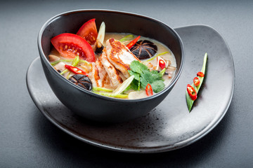 Chicken fillet in vegetable sauce in black dish.