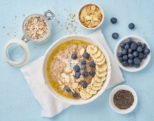Oatmeal with blueberries, banana on blue light background. Top view. Healthy diet breakfast