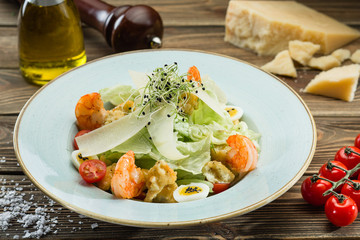 Salad with shrimps and vegetables and parmesan in a plate on a wooden table.