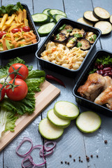 ready meal to eat in lunch boxes, raw vegetables around, food containers on wooden table