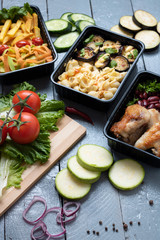 Fototapeta na wymiar ready meal to eat in lunch boxes, raw vegetables around, food containers on wooden table
