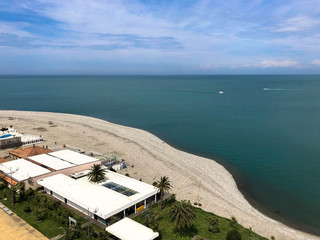Obraz premium Top view of the sandy beach with sand, sea, green palm trees and buildings, houses on a tropical warm summer resort, rest