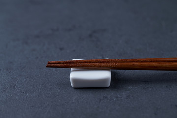 Wooden chopsticks and chopstick rest on black stone background. Close up. Copy space. 