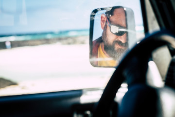 Fototapeta na wymiar Caucasian man face with sunglasses viewed in the mirror of the car - alternative people portrait - travel vehicle concept