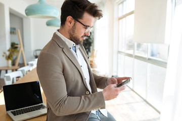 Handsome young business man using his smartphone while sitting on table in the office.