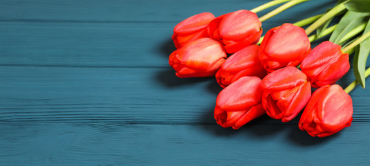 Many beautiful red tulips with green leaves and space for text on color wooden background, closeup