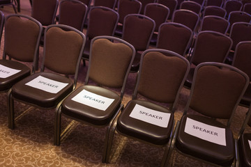 Brown chairs the conference hall before the event. First row for special guests. Inscriptions "speaker" on white sheets.