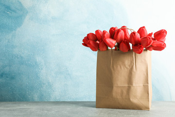 Paper bag with beautiful red tulips on table against blue background, space for text
