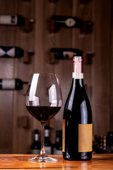Glass and bottle with delicious red wine on wooden table. In the background Red wine bottles stacked on wooden racks shot with limited depth of field.