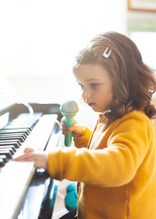 Fototapeta na wymiar Girl toddler plays with piano and toy microphone.