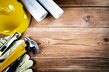 hammer, protective gloves, folding ruler, model knife, blueprint  and yellow safety helmet on wooden background