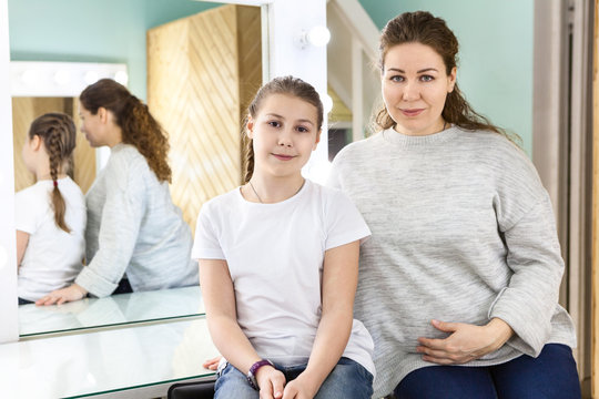 Portrait of mother and her teenager daughter sitting in dressing room, looking at camera