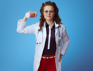 medical doctor woman with pink dumbbell showing biceps on blue