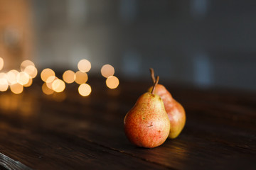 Beautiful ripe tasty pears on a large kitchen wooden table with a garland of lights. A beautiful...