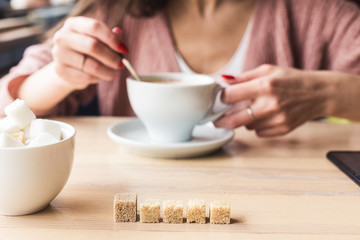Attractive young woman sits at a table in a cafe with a cup of coffee and mixes it with a spoon
