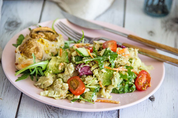 The concept of proper nutrition, keto diet, paleo diet. Salad with fresh vegetables and avocado, baked chicken breast with mushrooms and boiled egg on a pink plate, next to cutlery