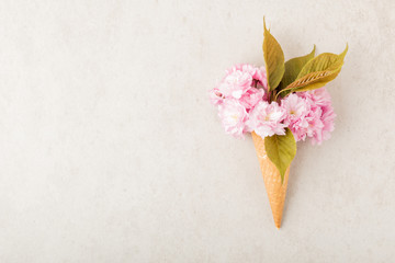Ice cream cone with blooming pink sakura flowers and green leaves. Top view, flat lay and copy space. Minimal summer concept