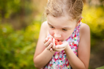 Blonde girl eating fresh raspberry. Farm concept, green summer background