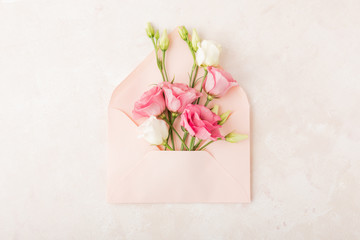 Creative layout with pink envelope and blooming flowers on pink background. Flat lay, top view with copy space. Minimal love, festive greeting or nature concept