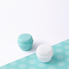 White and turquoise cosmetic bottle containers with decor, on white background top view flat lay.