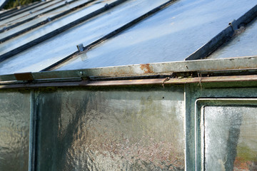 Garden shed closeup on a sunny day with shadows from trees. You see gardening items through the milk glass.