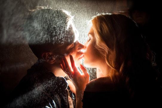 Love in the rain . Silhouette of kissing couple under umbrella
