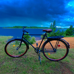 Fototapeta premium Adult road bike on the bank of a cloudy river.
