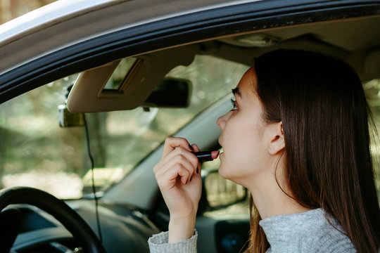 Girl makes up in a car holding a lipstick