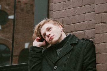young blond guy standing against the wall and holding a strand of hair, close-up portrait