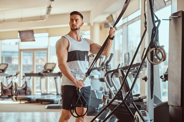 Fototapeta na wymiar Strong muscular man is posing next to training apparatus at sunny gym.