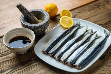 Raw saury on a white dish in the form of fish with lemon and herbs top view