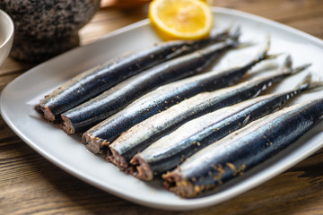 Raw saury on a white dish in the form of fish with lemon and herbs top view