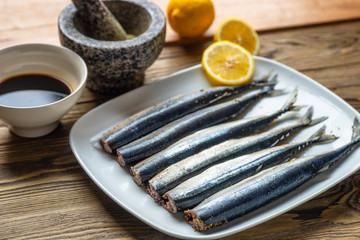 Raw saury on a white dish in the form of fish with lemon and herbs top view