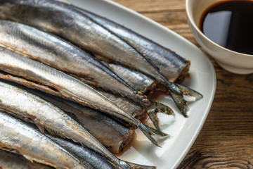 Raw saury on a white dish in the form of fish with lemon and herbs top view