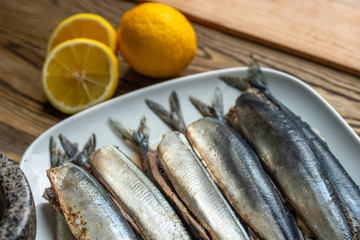 Raw saury on a white dish in the form of fish with lemon and herbs top view