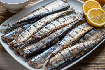 Smoked saury on a white dish in the form of fish with lemon and herbs