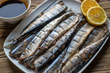 Smoked saury on a white dish in the form of fish with lemon and herbs
