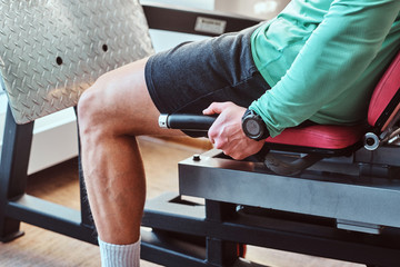Strong active man is doing legs exercises on training apparatus in gym