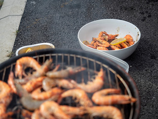 Cooked shrimp in a white bowl in focus, uncooked shrimps on a barbeque out of focus, Selective focus.