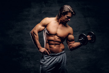 Fototapeta na wymiar Attractive muscular man is posing with dumbbell. He has naked torso.