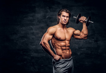 Fototapeta na wymiar Attractive muscular man is posing with dumbbell. He has naked torso.