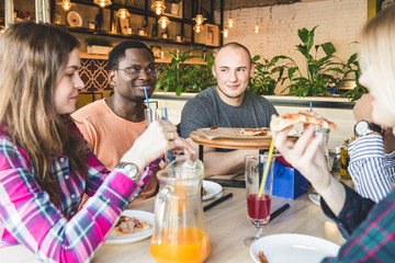 A company of multicultural  young people in a cafe eating pizza, drinking cocktails, having fun