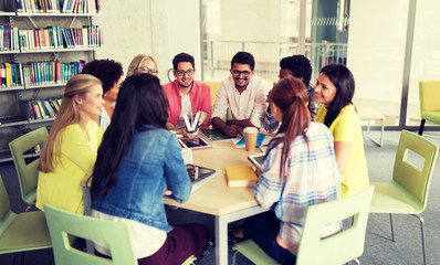 Obraz premium education, high school, learning, people and technology concept - group of international students sitting at table with tablet pc computers and books and talking at university