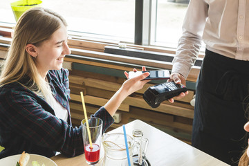 Young attractive woman paying in cafe with contactless smartphone payment