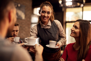 Happy waitress serving coffee to her guest in a cafe,