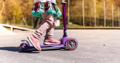 Girl with colorful dress with mobility scooter. Mädchen mit buntem Kleid fährt mit Tretroller.