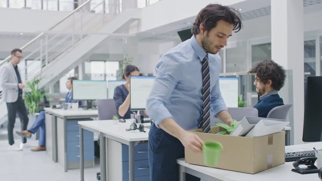 Sad Fired / Let Go Office Worker Packs His Belongings into Cardboard Box and Leaves Office. Workforce Reduction, Downsizing, Reorganization, Restructuring, Outsourcing. Mass Unemployment Market Crisis