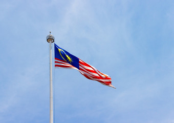 National flag of the Malaysia on a flagpole waving in the wind against a clean blue sky. Selective focus