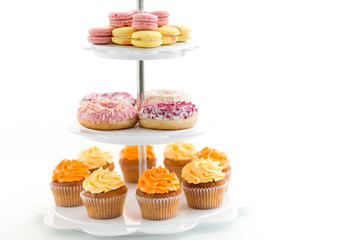 fast food and sweets concept - glazed donuts, cupcakes and macarons on stand over white background